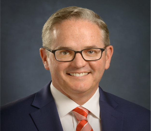 A person wearing a suit and tie smiling at the camera Description generated with very high confidence